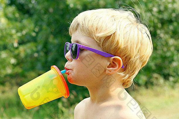 年轻的男孩穿紫色的太阳镜付小费头回来喝汁色彩斑斓的吸管杯阳光明媚的夏天一天