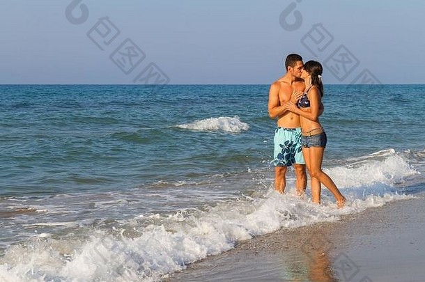 拥抱接吻年轻的夫妇短裤海滩装享受浪漫的光着脚走沙子海滩黄昏生活方式旅行假期概念
