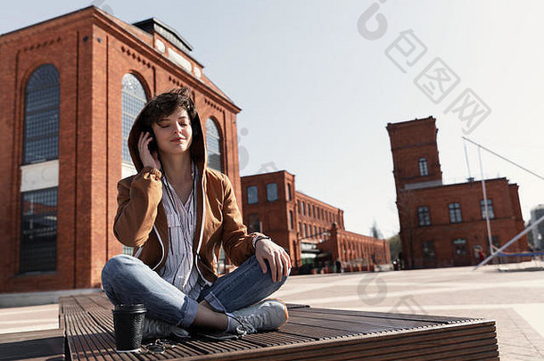 年轻的女孩时尚的短发型坐在板凳上听音乐耳机