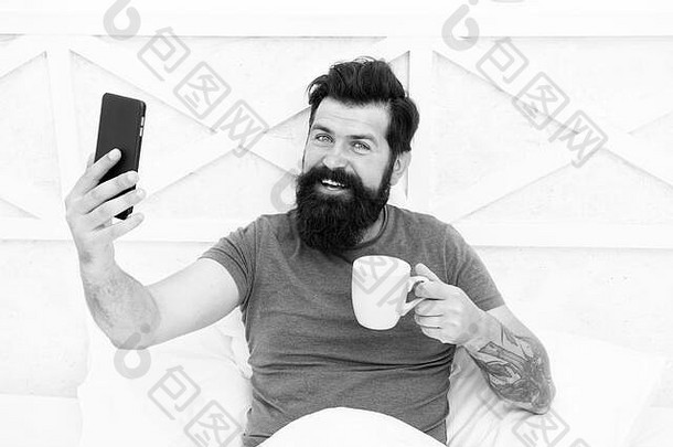 源能源有胡子的男人。享受视频会议咖啡床上快乐赶时髦的人持有杯移动电话热能源喝增加能源水平精力充沛的沟通能源提高