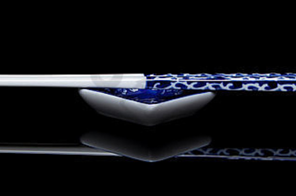 一对蓝色的白色筷子坐在匹配小碗项目反映了黑色的闪亮的表面全景形式