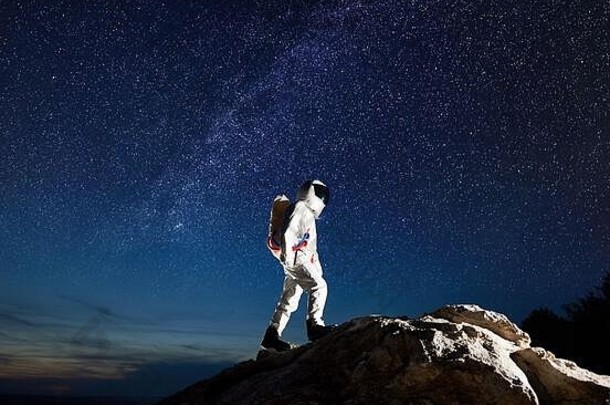 完整的长度空间旅行者攀爬岩石山惊人的晚上天空星星宇航员空间西装达到前巨大的岩石概念乳白色的空间探索