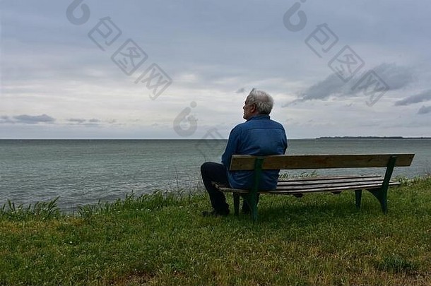 上了年纪的男人。坐着木板凳上多云的一天考虑怀旧海景