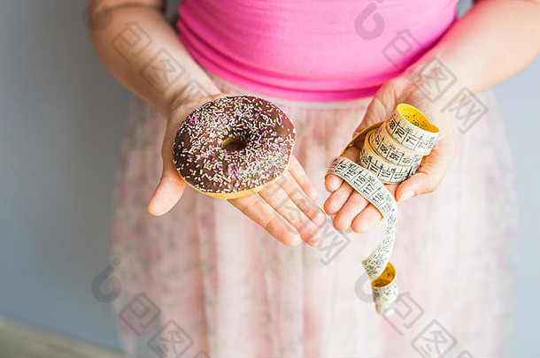 特写镜头女人的手持有甜甜圈测量磁带概念健康的吃饮食