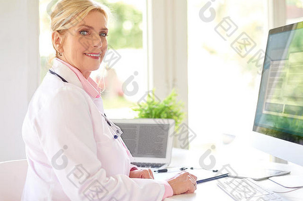美丽的微笑女研究医生坐着前面电脑医生的办公室工作