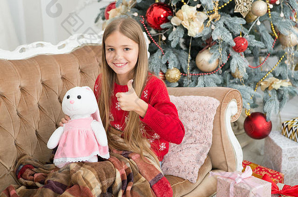 女孩拇指可爱的兔子圣诞节树小女孩持有兔子玩具孩子玩软玩具小孩子快乐微笑现在圣诞节玩具