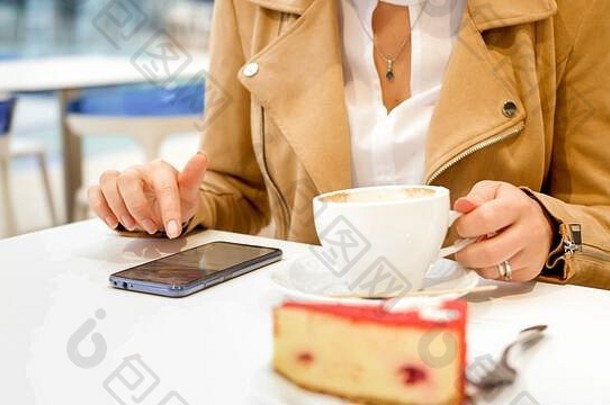 特写镜头照片年轻的女人持有杯咖啡打字消息智能手机咖啡馆