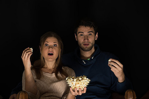 年轻的夫妇男人。女人坐着黑暗房间前面看电影吃爆米花显示情绪