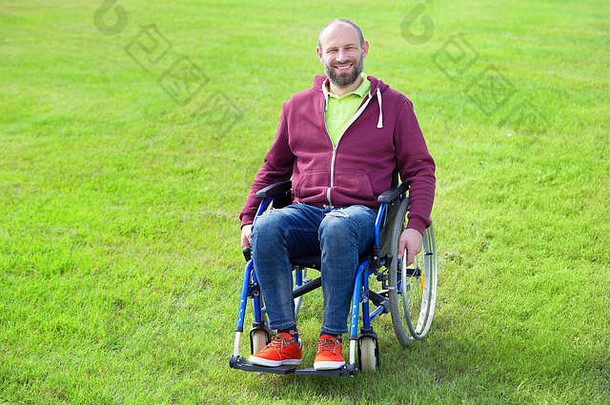 快乐微笑年轻的成人男人。轮椅站绿色草