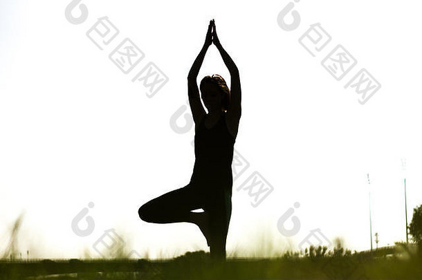 年轻的运动女人练习哈达瑜伽绿色场多叶的草河城市背景