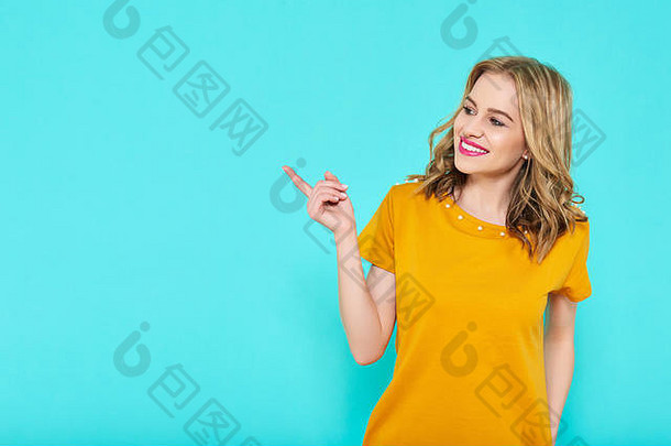 时尚的有吸引力的年轻的女人穿芥末颜色夏天衣服摆姿势柔和的蓝色的背景前面视图微笑女人指出手指