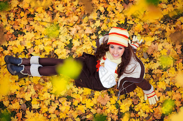 年轻的女人坐着黄金秋天叶子前视图