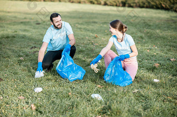 快乐男人。女人志愿者穿着蓝色的t恤清洁公共花园塑料垃圾袋