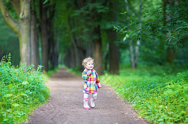 有趣的卷曲的婴儿女孩雨靴子走公园