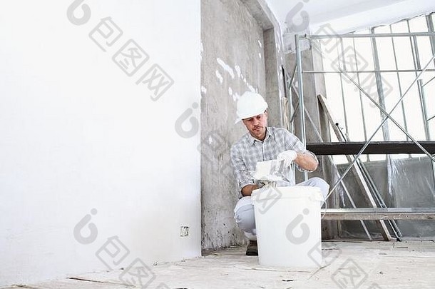 粉刷工男人。工作砂浆桶抹墙室内建设网站穿头盔保护手套梯