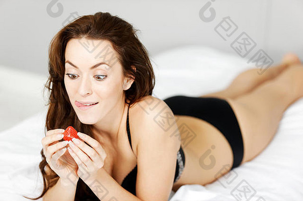 美丽的年轻的女人享受新鲜的草莓床上黑色的内衣