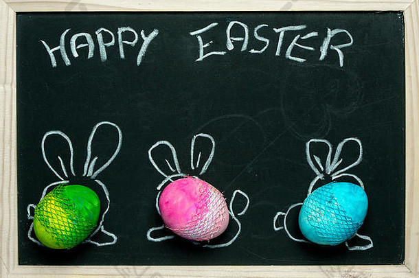色彩斑斓的柔和的复活节<strong>鸡蛋</strong>画兔子耳朵背景黑板上