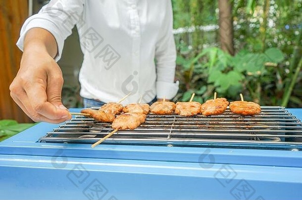 亚洲白色t恤女孩持有铺设烤猪肉坚持蓝色的烧烤炉子机前面户外模糊树花园背景