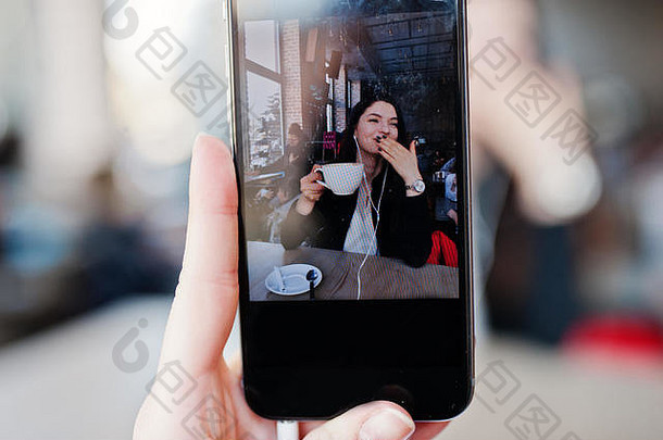 关闭照片屏幕移动手机浅黑肤色的女人女孩坐着咖啡馆杯卡布奇诺咖啡听音乐耳机