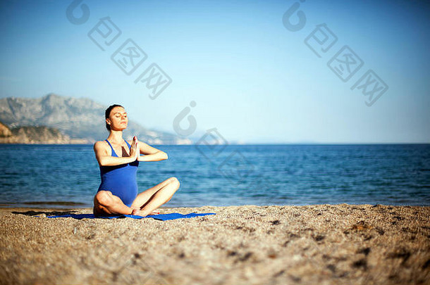 年轻的怀孕了女人享受瑜伽冥想海滩