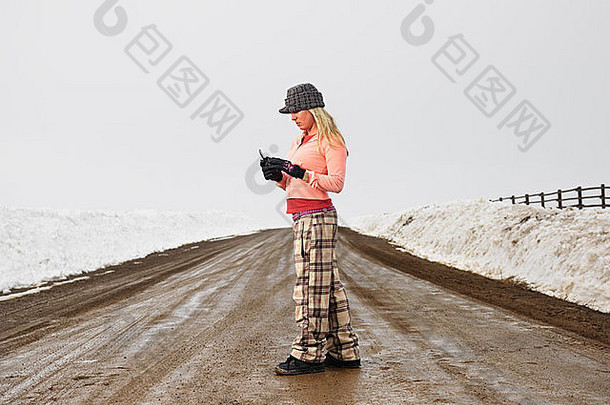 年轻的女人冬天衣服站泥泞的污垢路细胞电话