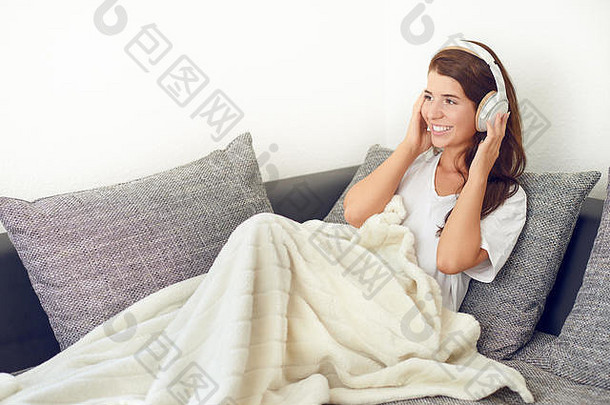 微笑快乐有吸引力的活泼的年轻的女人放松灰色沙发地毯腿听音乐立体声耳机