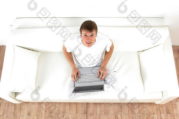 高角视图年轻的快乐男人。沙发移动PC
