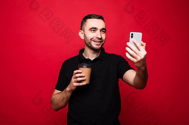 肖像快乐的英俊的年轻的男人。站孤立的红色的背景持有外卖咖啡杯采取自拍