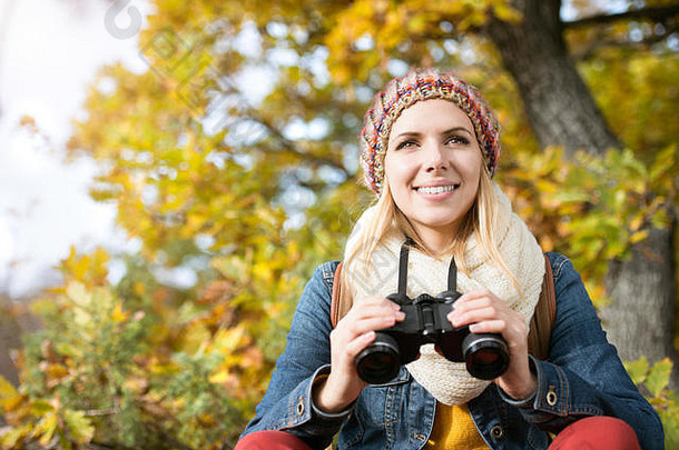 美丽的年轻的女人持有双筒望远镜色彩斑斓的阳光明媚的秋天
