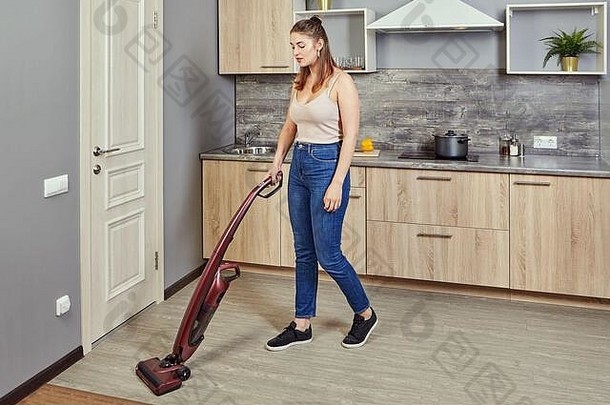 年轻的高加索人女人真空吸尘器厨房地板上无线垂直真空更清洁的电扫帚女仆清洁旅馆烹饪