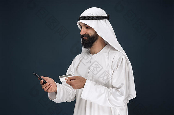 肖像阿拉伯沙特商人黑暗蓝色的工作室背景男人。智能<strong>手机支付</strong>比尔在线购物押注概念业务金融面部表达式人类情绪