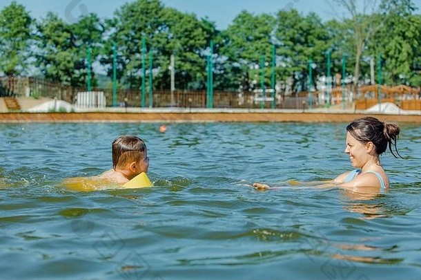 蹒跚学步的男孩充气臂章艾滋病玩水妈妈。湖水