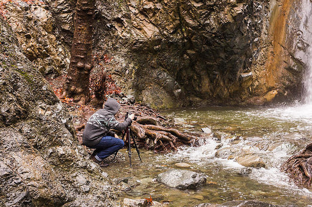 年轻的摄影师背包使照片瀑布岩石相机地中海海