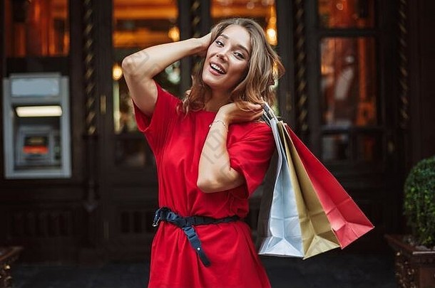年轻的快乐的女人<strong>红色</strong>的衣服快乐相机持有色彩斑斓的购物袋手大通过背景