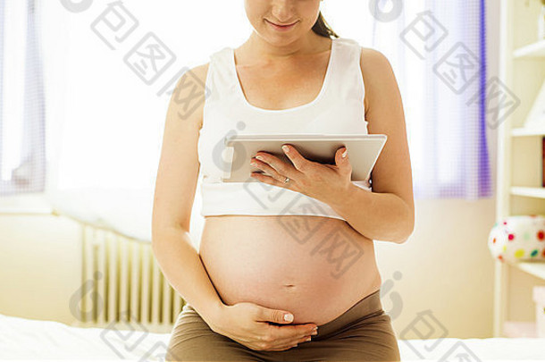 美丽的怀孕了女人数字平板电脑卧室