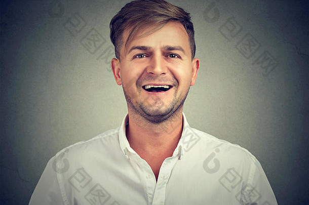 肖像英俊的年轻的男人。白色衬衫笑积极相机灰色的背景