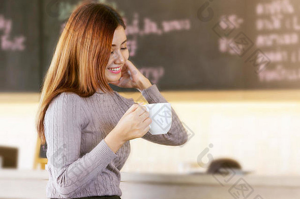 微笑女人杯咖啡手坐在现代咖啡馆