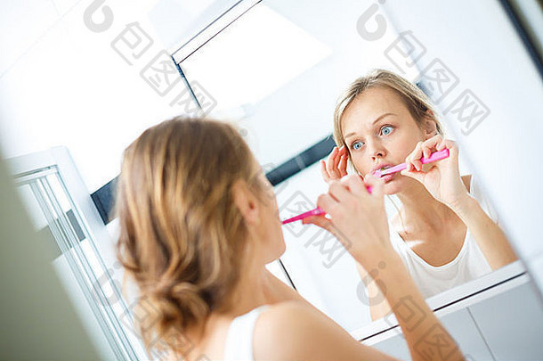 漂亮的女刷牙牙齿前面镜子早....使愚蠢的脸检查皮肤