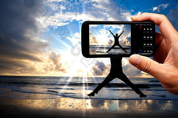 相机移动电话快乐跳男人。海滩美丽的日出