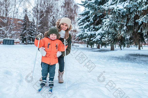 年轻的快乐妈妈。女人持有男孩年儿子学习滑雪冬天公园有爱心的婴儿提高孩子温暖的
