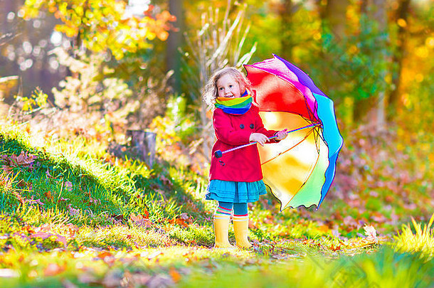 可爱的卷曲的女孩穿温暖的红色的外套雨靴子玩色彩斑斓的伞享受阳光明媚的秋天一天