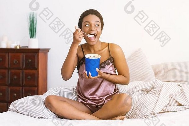 有趣的糖果非洲美国女孩睡衣吃冰奶油桶床上