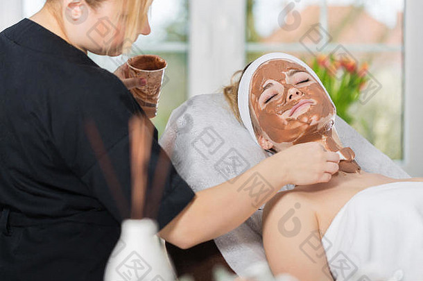 美容师应用让人耳目一新巧克力面具年轻的女人的脸