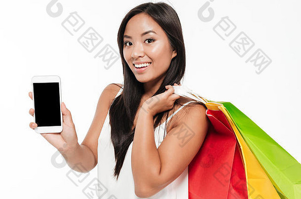 肖像微笑年轻的亚洲女人显示空白屏幕移动电话站色彩斑斓的购物袋孤立的白色背景
