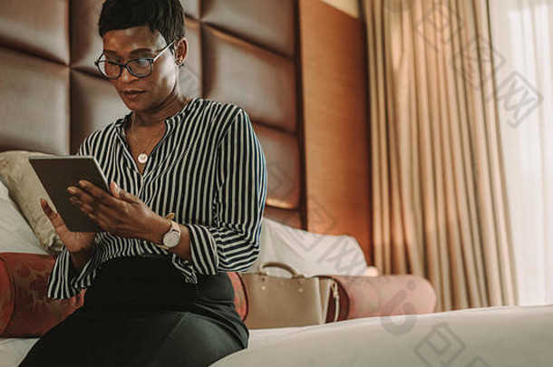 女商人坐着床上数字平板电脑非洲女人业务旅行工作酒店房间