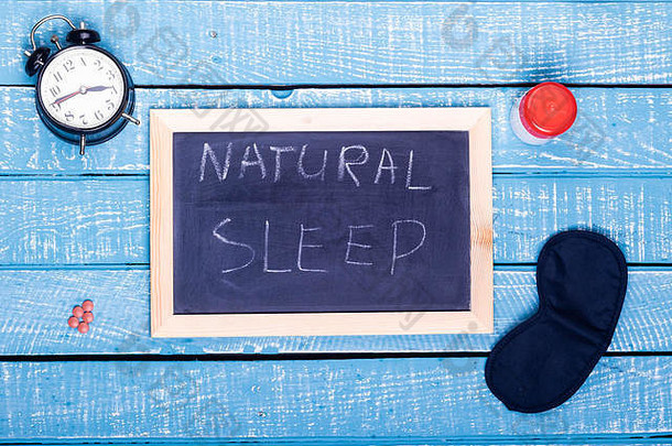 睡眠概念显示报警时钟睡觉药片眼睛面具黑色的董事会阅读自然睡眠饱经风霜的蓝色的背景