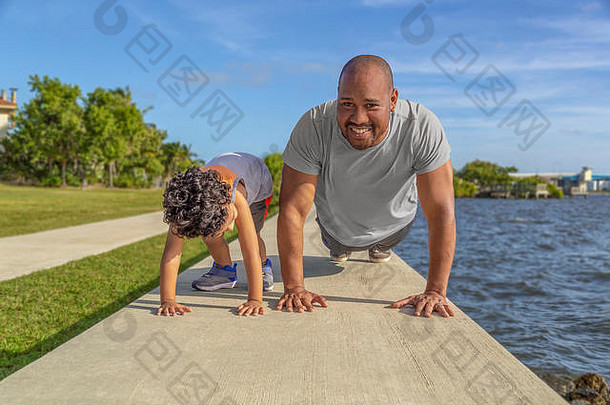 父亲微笑显示儿子俯卧撑海堤两岸间的男孩爸爸教学锻炼好健康