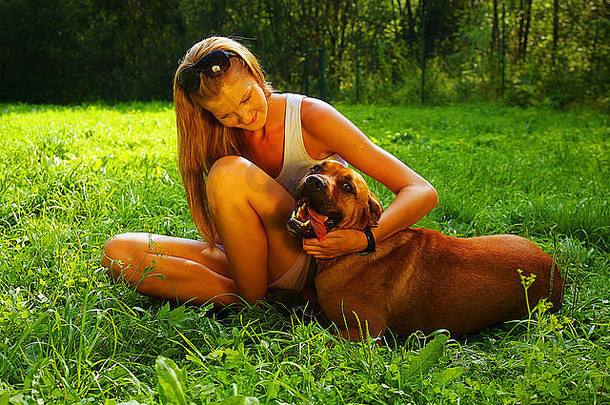 年轻的美丽的女人金发女郎头发玩mastif狗后院绿色草