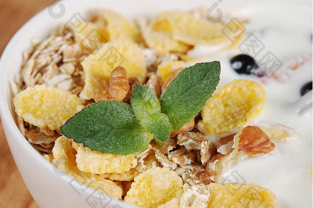 燕麦小麦玉米片坚果酸奶薄荷叶子小白色碗木背景