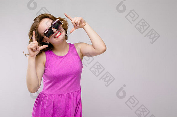 迷人的年轻的女孩粉红色的衣服灰色的背景快乐的女孩广场眼镜女孩点手指前